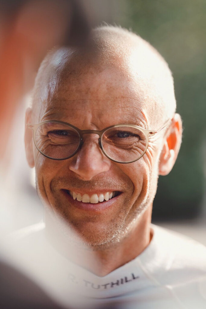 Man with round glasses and a white shirt smiling with blurry background