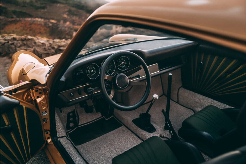 black minimal interior with beige carpeting and black steering wheel and stick shift of a gold car