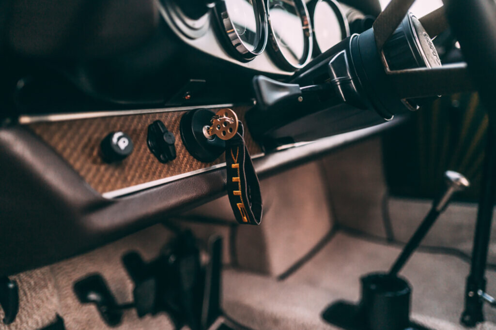 closeup of black and brown dashboard of a car with simple carpet flooring and a key in the ignition with a orange and black jet tag