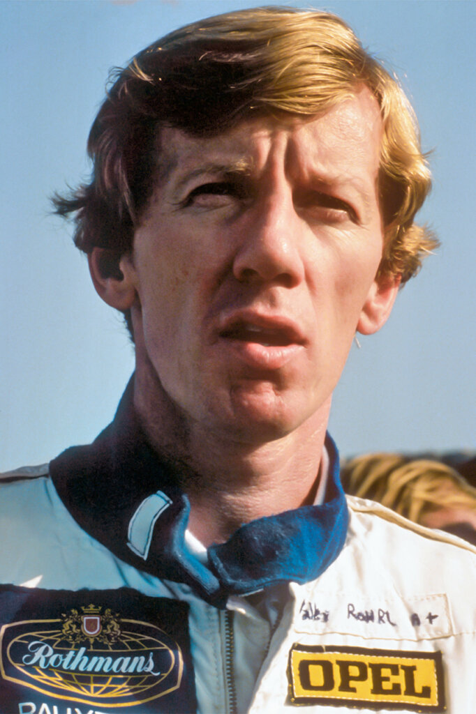 Man with blonde hair with a race suit on with a blue collar with clear blue sky in background