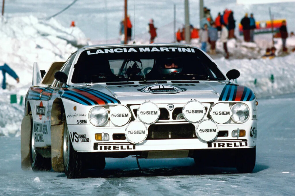 Lancia Martini car driven in the snow with a crowd of people behind them