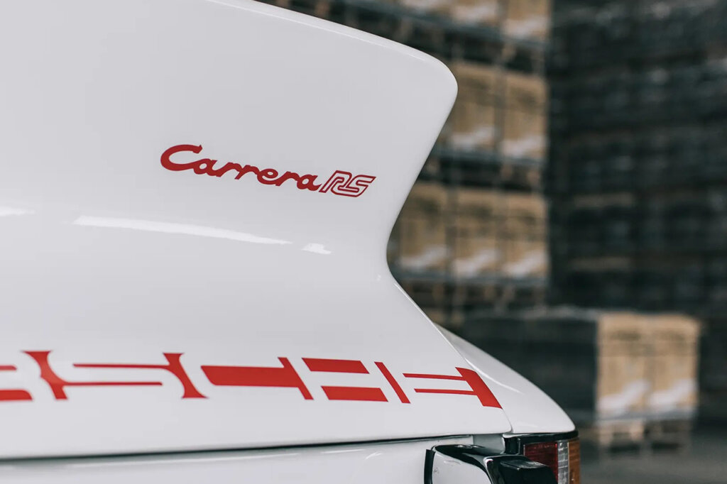 Closeup of red badging on the rear end of a 911 Carrera RS with boxes in the background out of focus