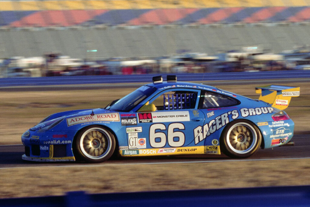 Blue 996 GT3 RS race car with race livery and the number 66 on the door and a yellow wing driving on a racetrack