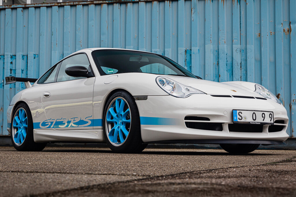 white Porsche 911 996 GT3 RS with light blue accents parked in front of a light blue shipping container. 