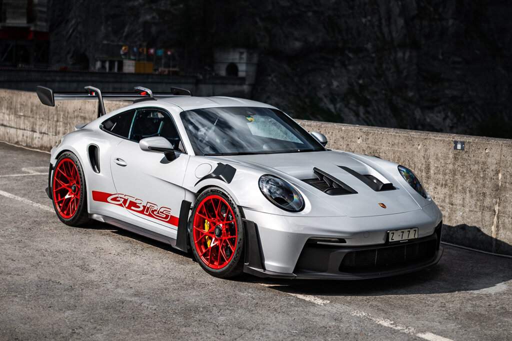 White 992 GT3 RS with red wheels parked on a bridge with mountains in the background