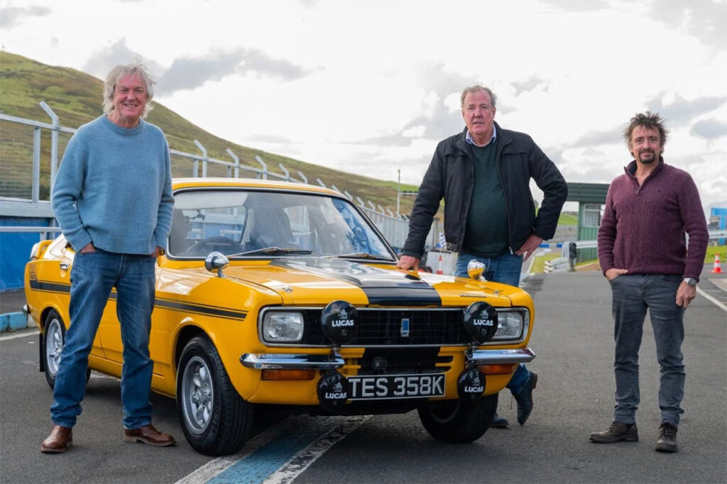 Yellow and black Avenger Tiger race car with three men standing next to it with cloudy sky in background