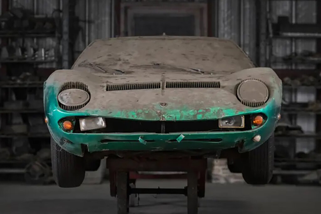 Dust covered Lamborghini with large circular headlights and orange and clear auxiliary lights positioned under these on the grill of the car