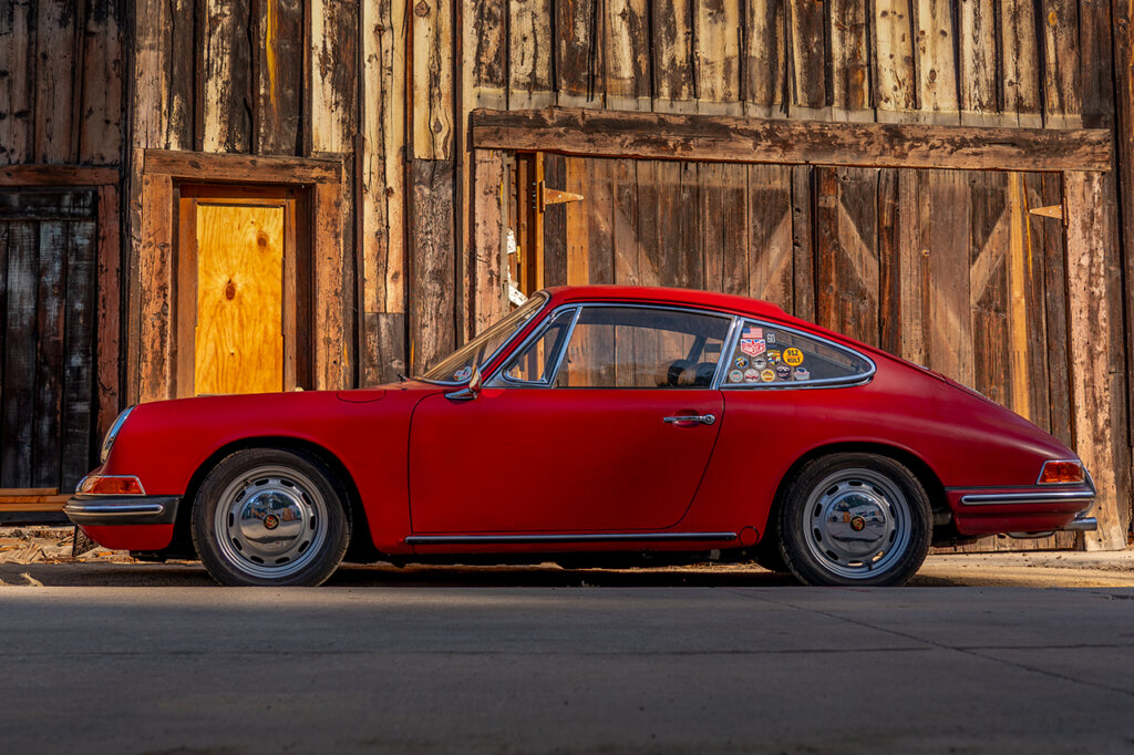Red Porsche 912 parked in front of a wooden structure with a light brown door