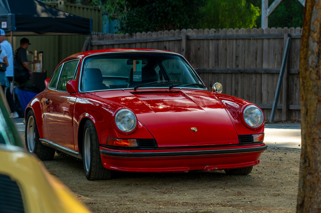 Red Porsche 911 parked on the dirt next to a tree and a yellow car