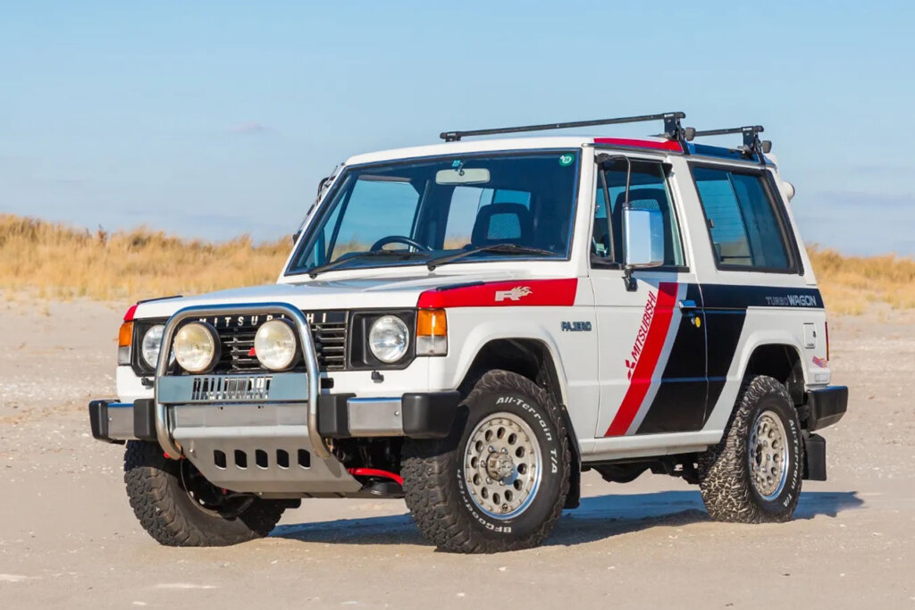 White, red and black Mitsubishi Pajero parked on a sandy dune with blue sky in the background