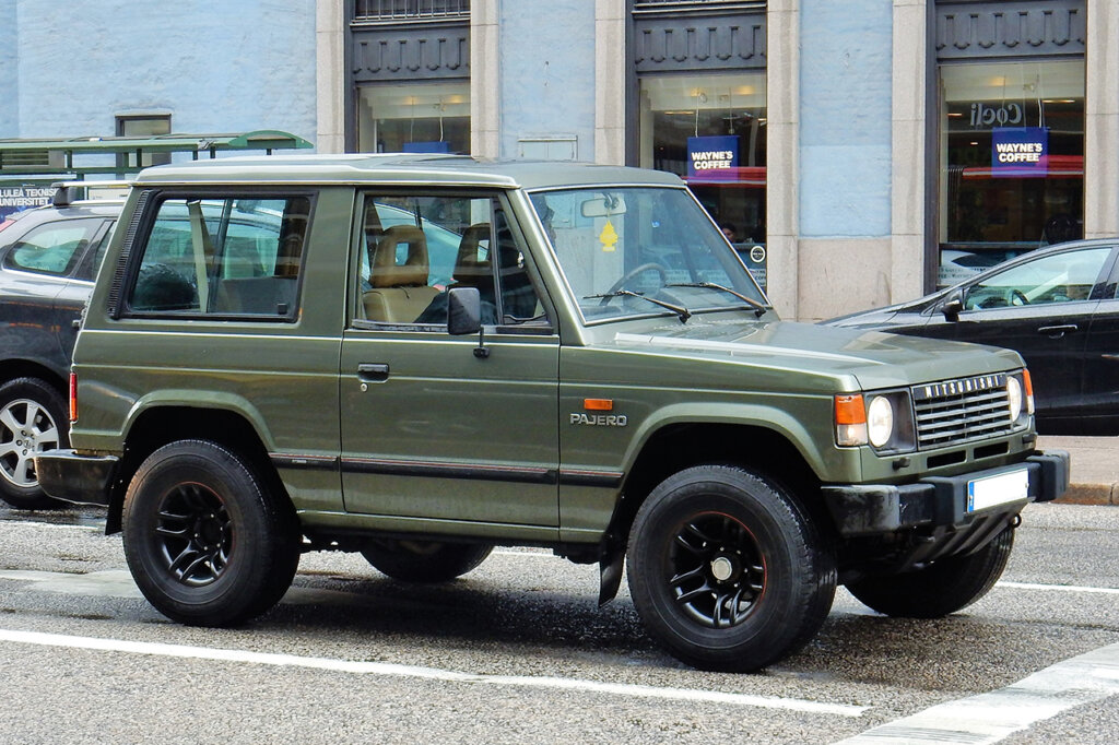 Green Mitsubishi Pajero parked on the street with buildings in the background