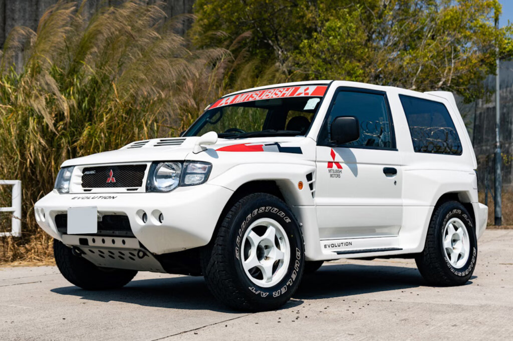 White and red and green Mitsubishi Pajero parked on a driveway with trees in the background
