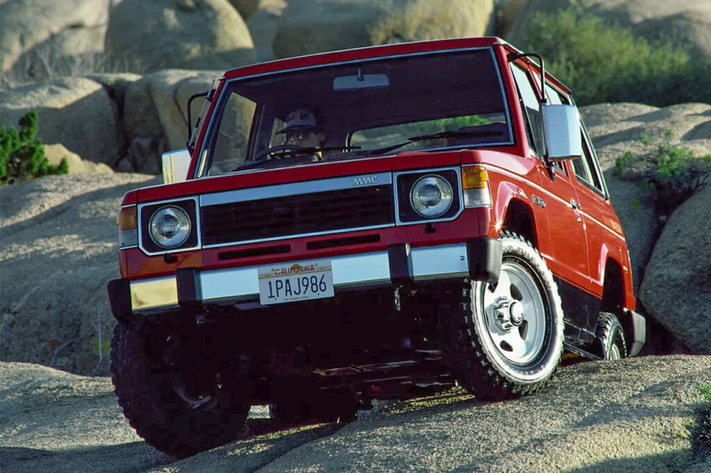 Red Mitsubishi Pajero crawling over a rock with a man in the drivers seat