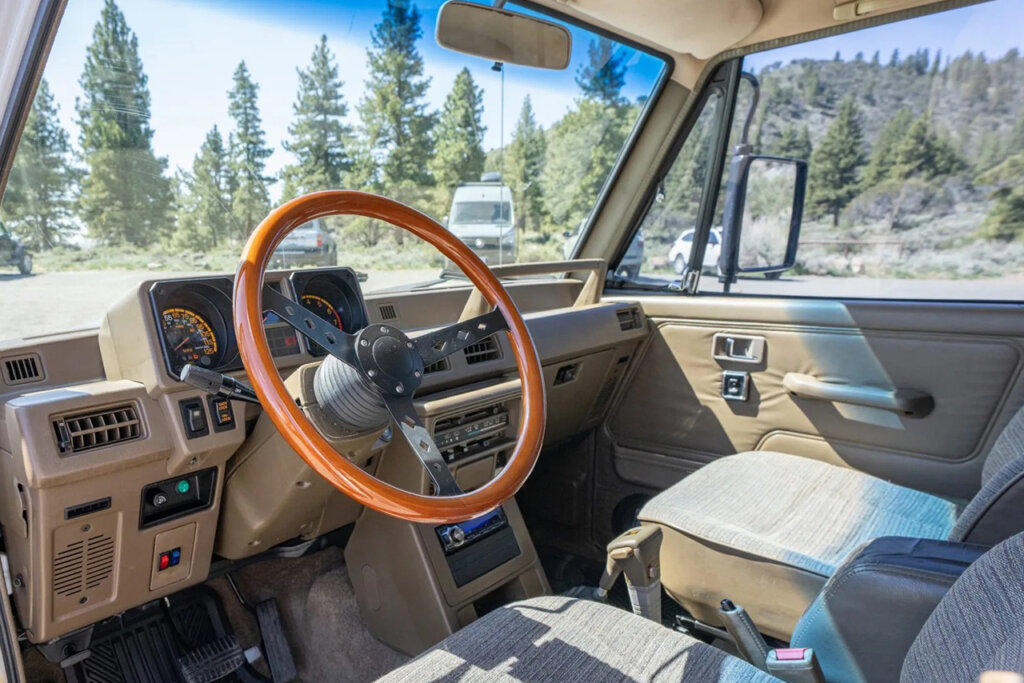 Wood grain steering wheel with beige suede seats of a mitsubishi suv car with trees in the background