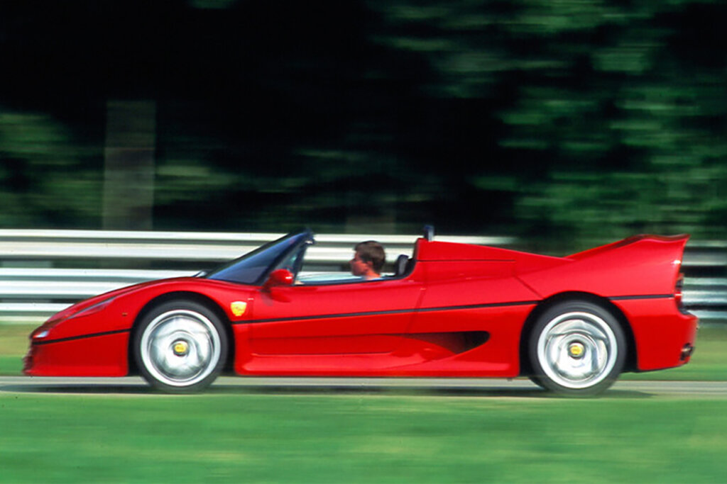 Red Ferrari F50 with a man behind the wheel with green grass on either side of the car