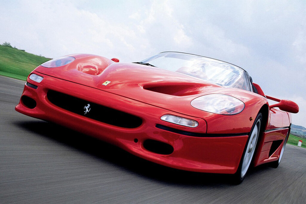 Red Ferrari F50 driving fast on a road with clouds in the sky