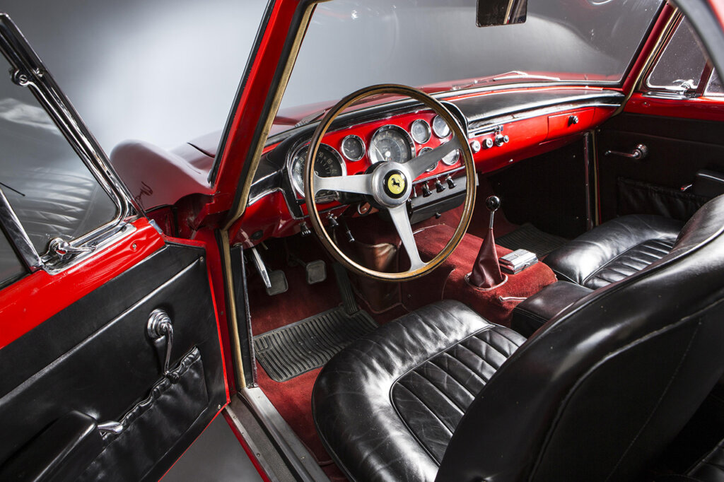 Black interior with black leather seats, black leather door cards and a simple brown wood grain steering wheel with the Ferrari logo on the horn button