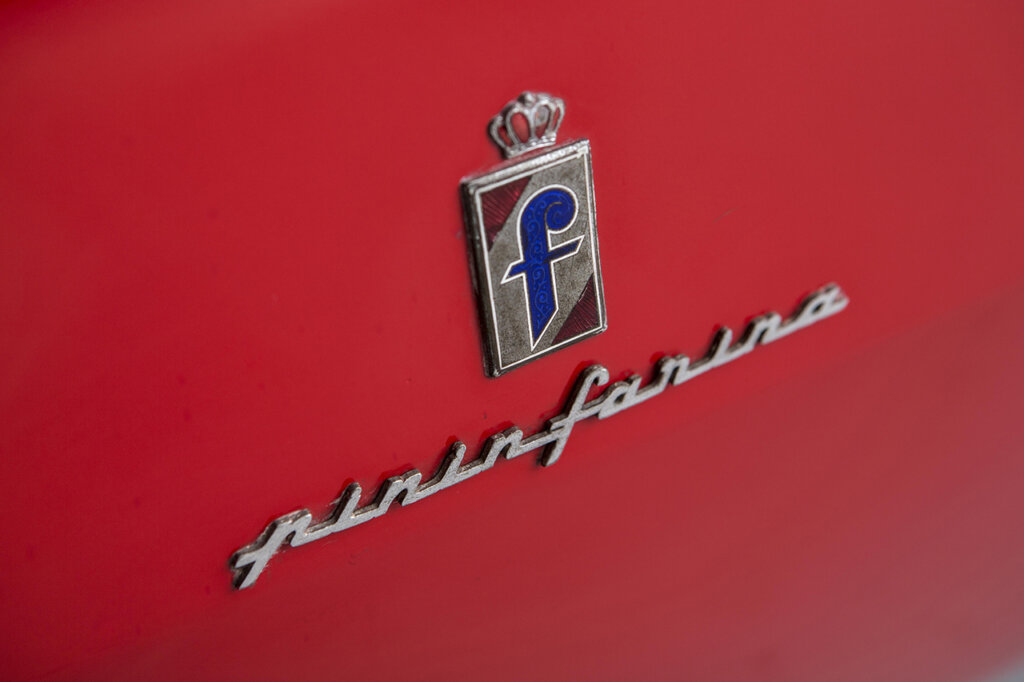 Blue and grey rectangular shield above a cursive word that says Pininfarina on a red car