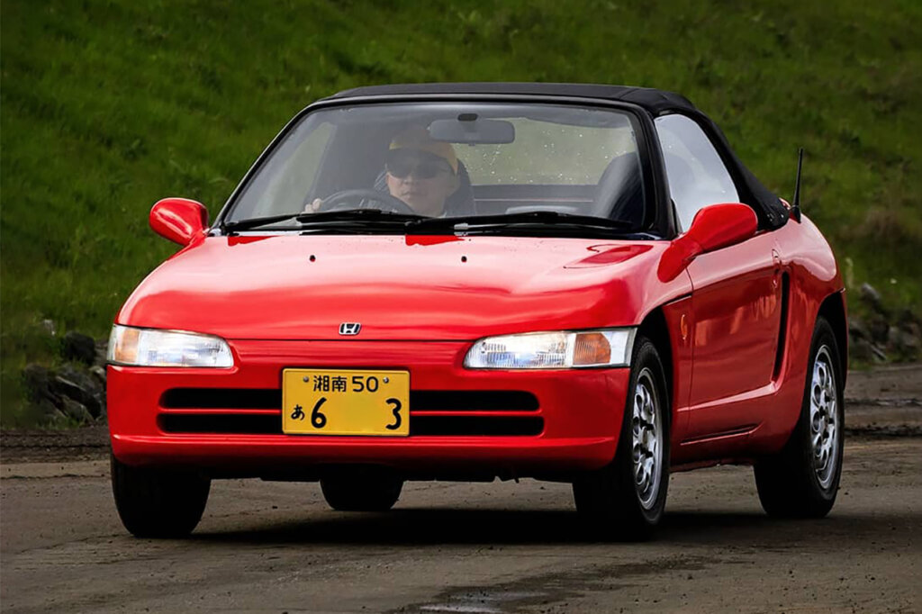 Red Honda Beat with a man behind the wheel with a yellow license plate, driving on the road