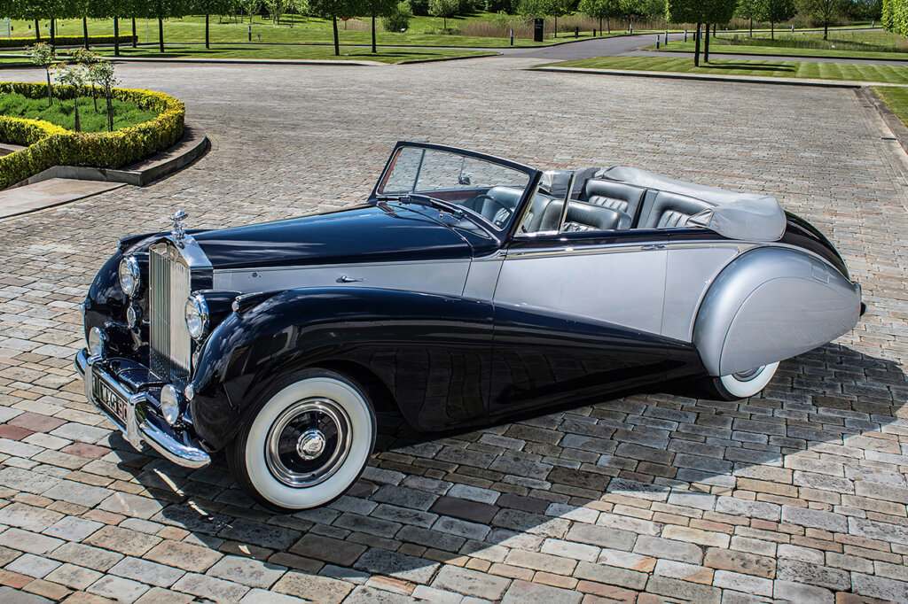 Blue and silver Rolls Royce Silver Dawn car parked on a brick driveway with grass surrounding it