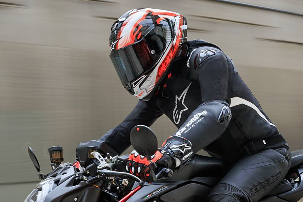 Motorcycle rider in full Alpinestars saftey jacket, pants, gloves & boots riding fast on a black bike with circular side mirrors