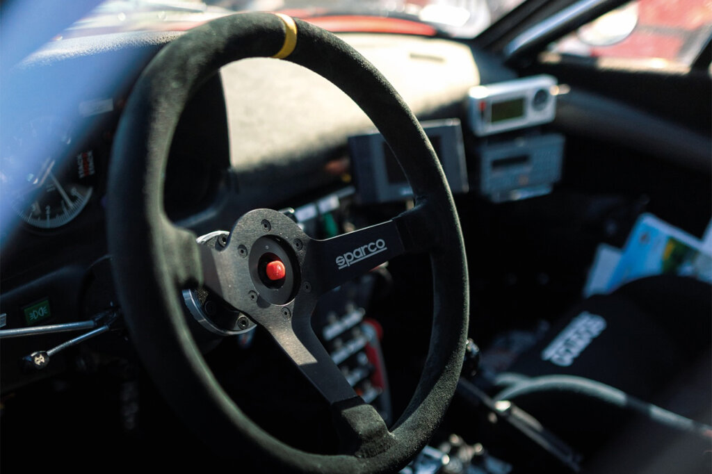 Black suede Sparco steering wheel with a red button in the middle of the wheel of a modified car