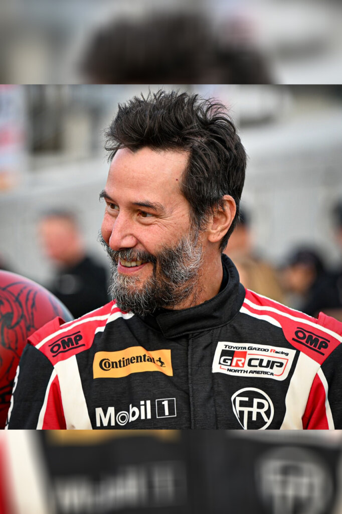 Man smiling with a race suit on with many sponsors like OMP racing which is present on both shoulders