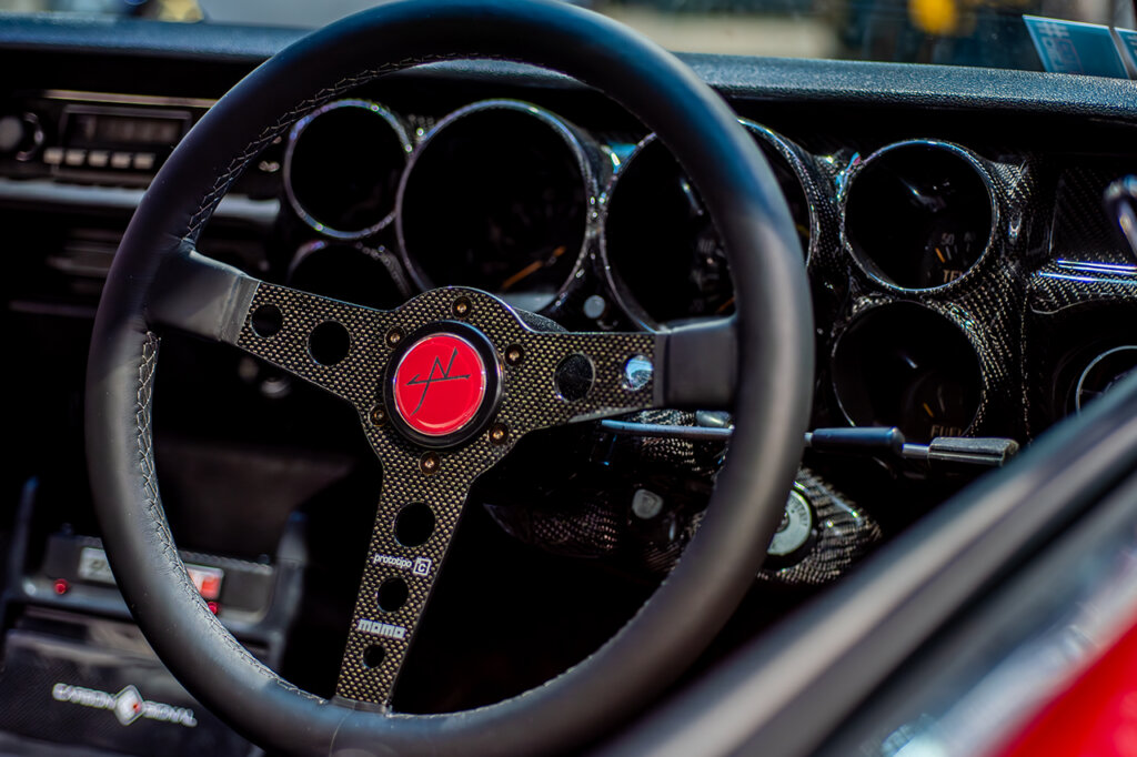 Black with red horn button MOMO steering wheel of a modified car that has carbon fiber trim