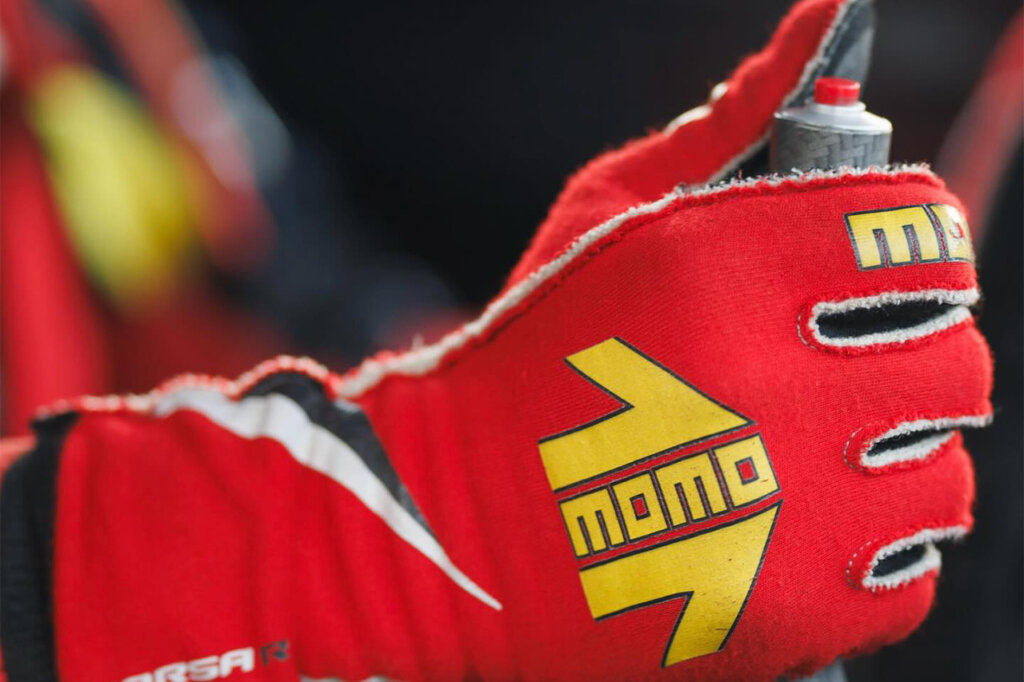 A person wearing Red MOMO racing gloves and holding a starter in his hand getting ready to push the red button