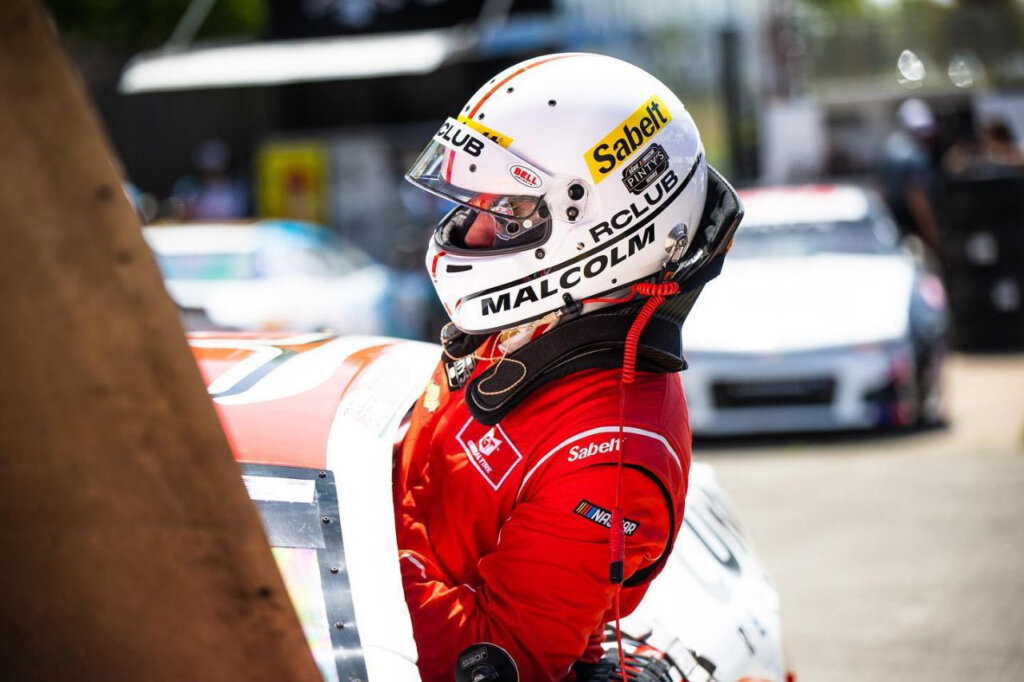 Sabelt Helmet gear of a race car driver getting into a car through the window, with cars in the background