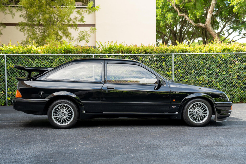 Black RS500 Cosworth parked in front of a fence and green shrub parked on a black asphalt