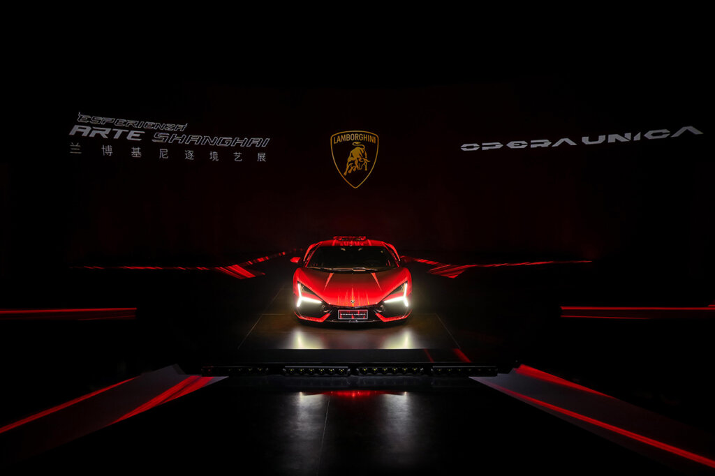 Red Lamborghini Revuelto Opera Unica parked on a stage with red accents and the Lamborghini logo and branding on the screen behind it.