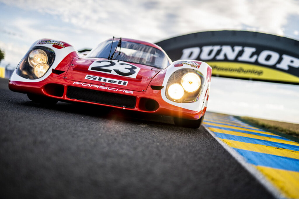 Red #23 Porsche 917 closeup on the racetrack with the Dunlop tire signage in the background.