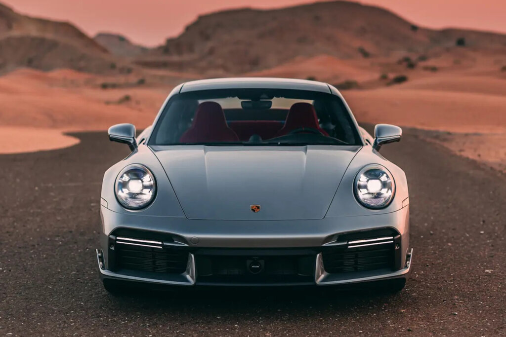 Silver 911 parked in the center of the road with brown hills and sand in the background