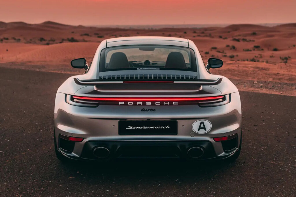 Shot of a silver 911 shot from behind with open land with brown hills and dirt in the background