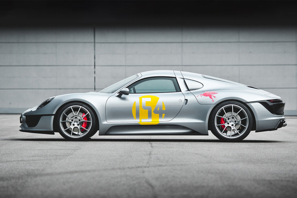 Porsche Le Mans Living concept car side profile with yellow number on the door with red brake calipers and a low profile height parked in front of a white brick wall.