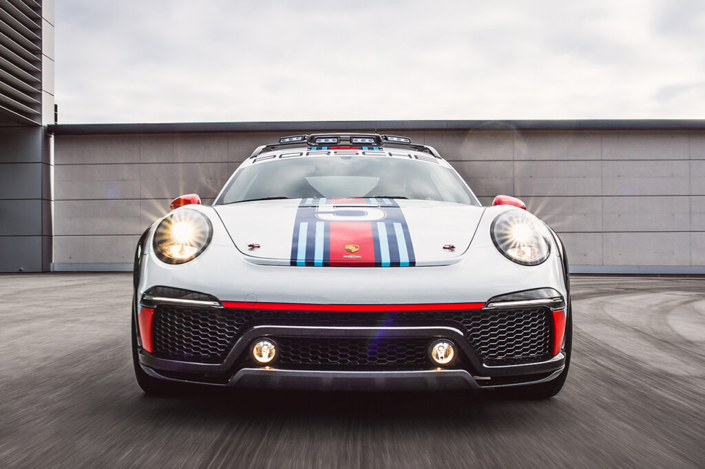 Martini livery on a Porsche Vision Safari concept car driving fast towards the camera with a brick wall behind it.