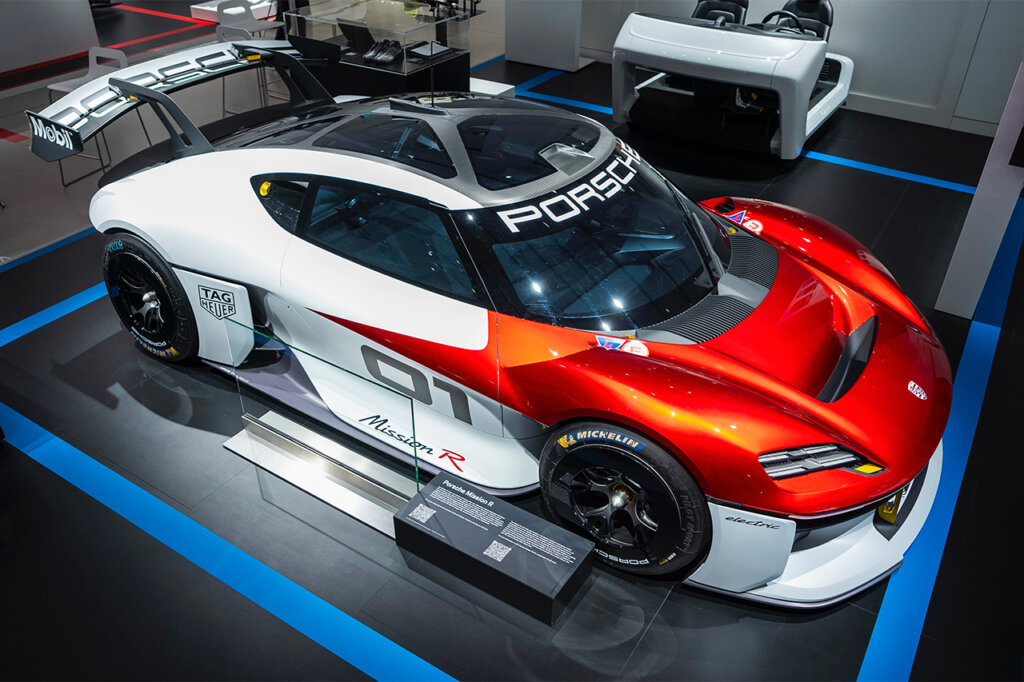 White Porsche Mission R with red bonnet and a large rear mounted wing parked on a platform inside of a room.