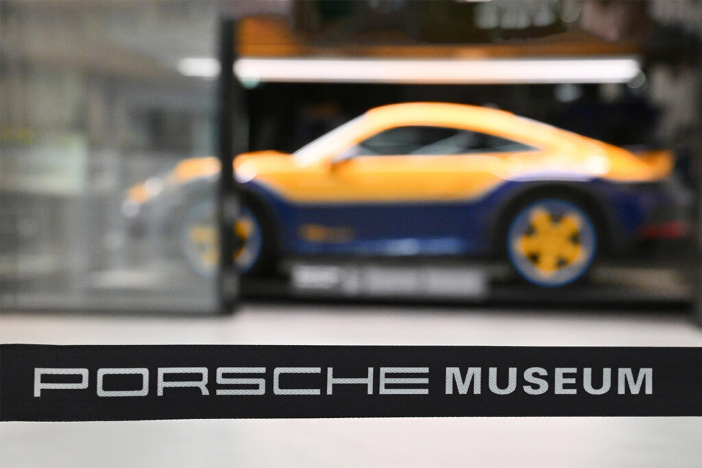 blurry focus on a yellow and blue Porsche 911 with a band going across the bottom of the photo with the words Porsche Museum in white.