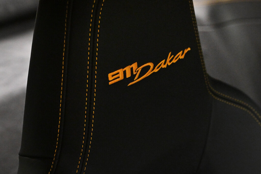 Black suede seat with yellow stitching and an embroidered 911 Dakar badge