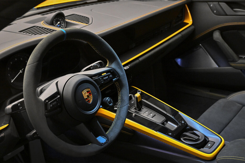 Porsche 911 interior with yellow accents and a steering wheel with the Porsche crest.