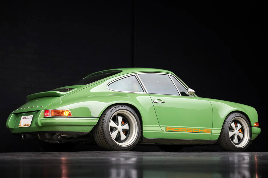 Green Singer Porsche 911 pictured in a dark room with reflective floor and black background.