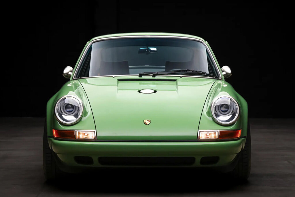 Front end photo of a green Singer Porsche with large single round headlights in a dark room.