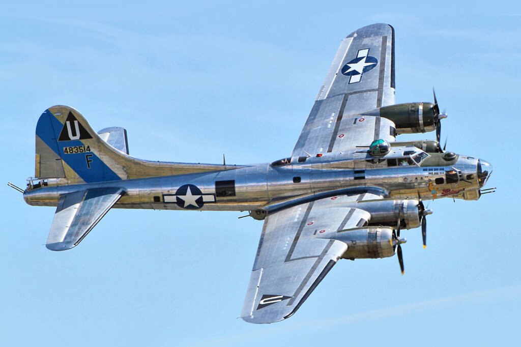Silver chrome Flying Fortress B-17 air craft flying through the blue sky.
