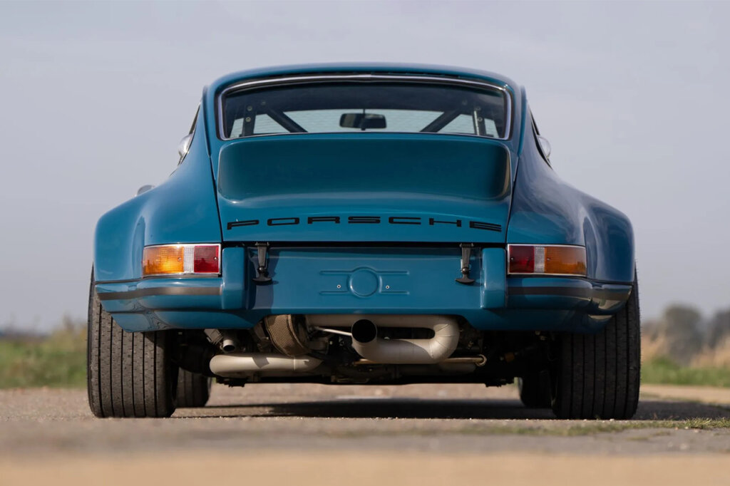 Blue Porsche 911 930 with a turbo peeking under the rear bumper attached to the exhaust and the car is facing away from the camera.