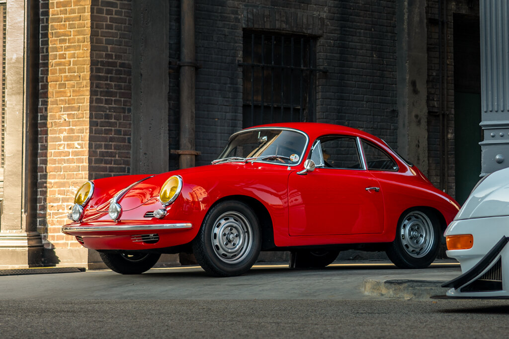 Red Porsche 356 parked in an alley way in front of a white car