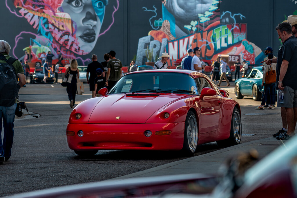 Red Porsche 911 964 Strosek car parked near people walking with a large Frankenstein mural in the background
