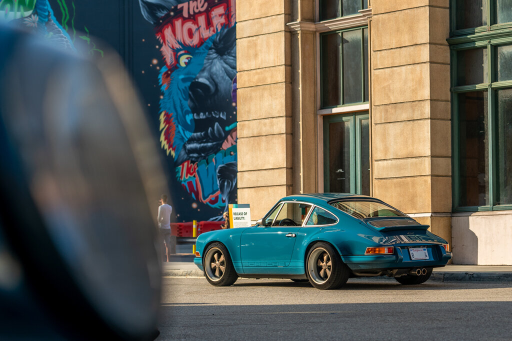 Teal 911 parked on the side of the road next to a building with a cartoon in the distant background