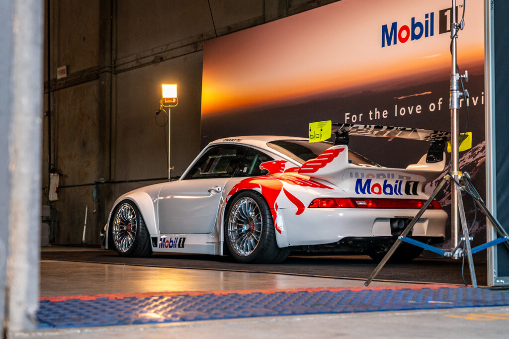 White and red 993 GT2 positioned next to a Mobil 1 banner backdrop in a garage