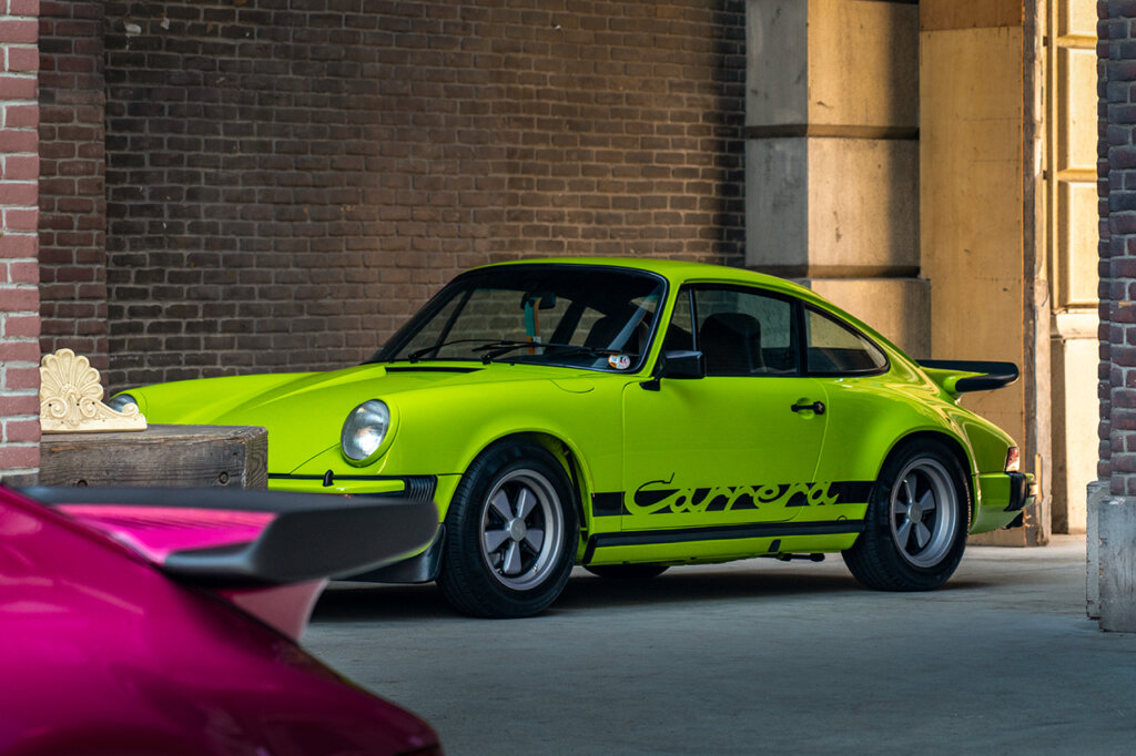 Neon Green 911 Carrera parked next to a brick wall with a purple Porsche 930 wing in front of the car
